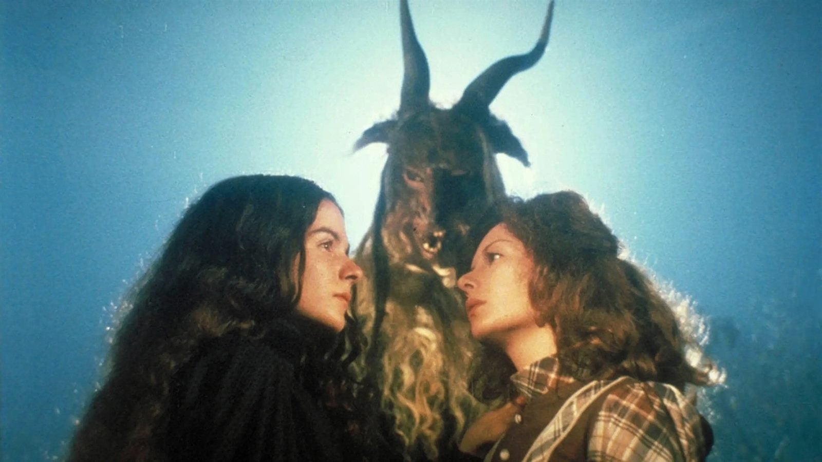Dos jóvenes frente a frente y, detrás, una figura con cuernos de macho cabrío sobre un cielo azul, en Alucarda (1977)