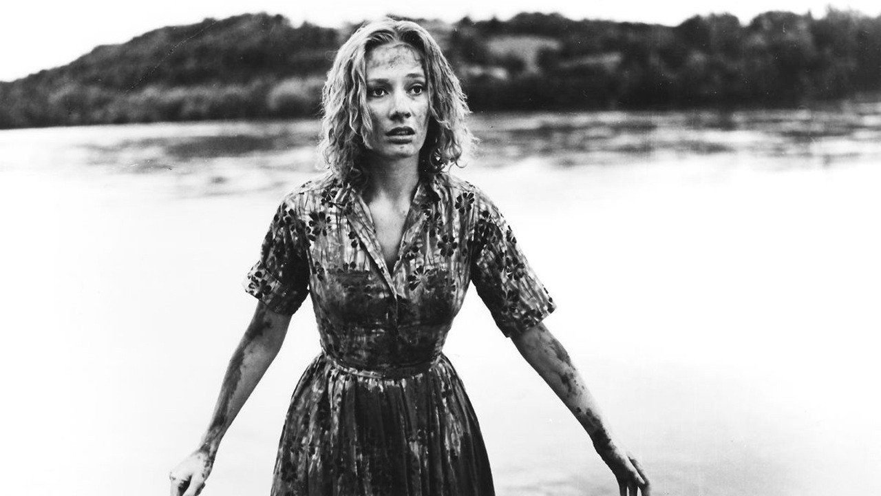 Una mujer rubia con el vestido empapado sale de un río, con la orilla boscosa al fondo, en Carnival of Souls (1962)