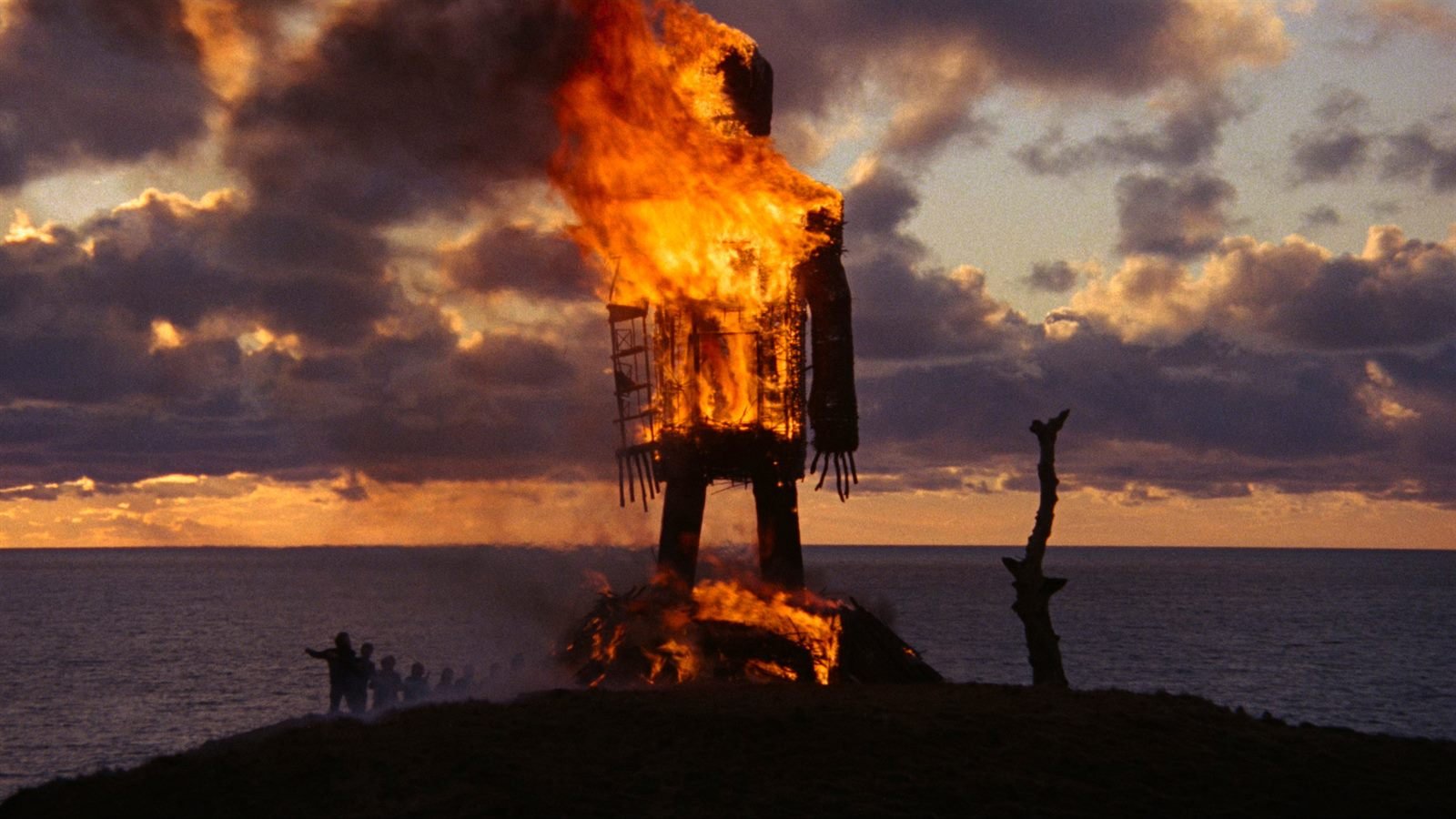Un gigantesco hombre de mimbre arde sobre un acantilado al atardecer, con el mar al fondo, en El hombre de mimbre (1973)