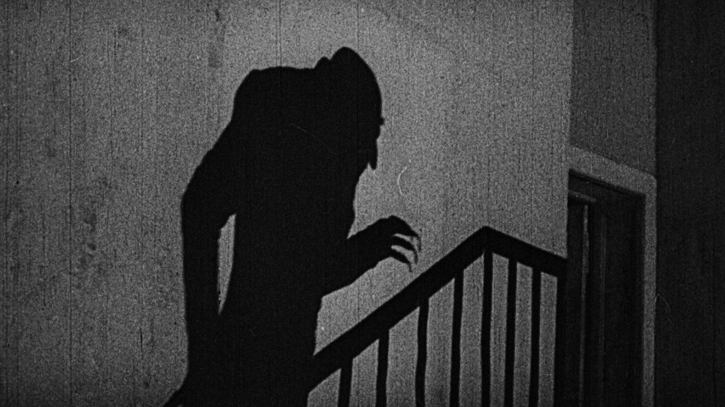 La sombra de una figura encorvada de garras largas sube por una escalera, en Nosferatu (1922)