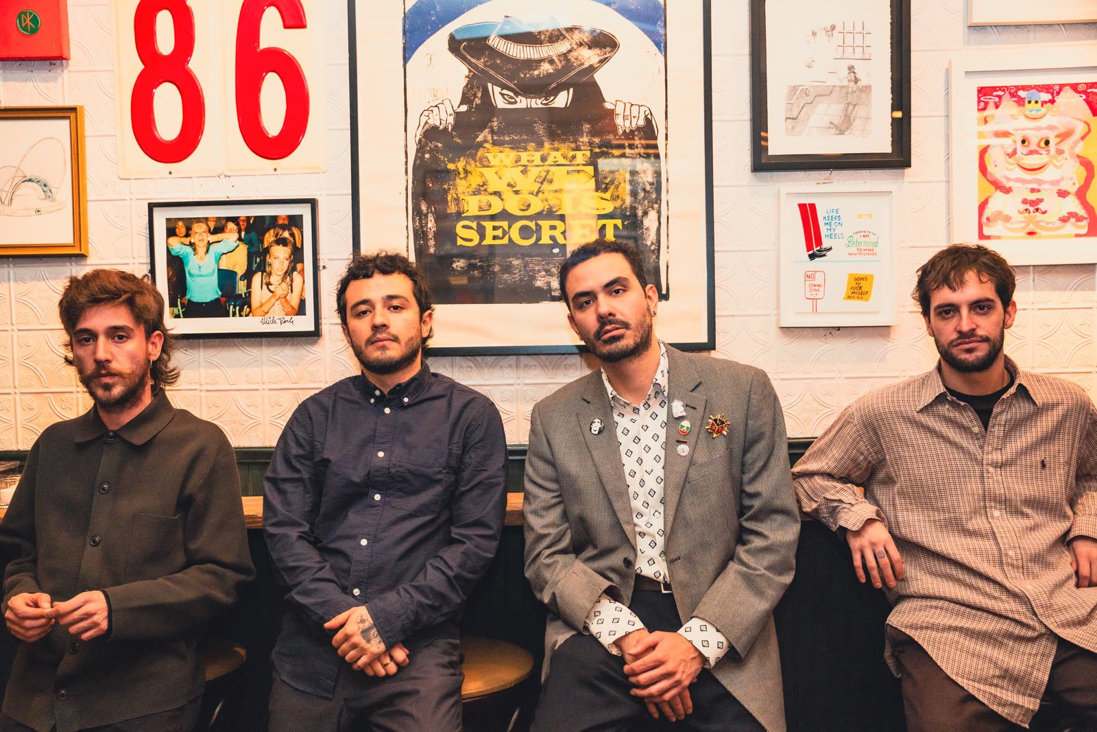 Cuatro integrantes de la banda mexicana The Shelter sentados en fila frente a una pared de carteles y fotografías enmarcadas