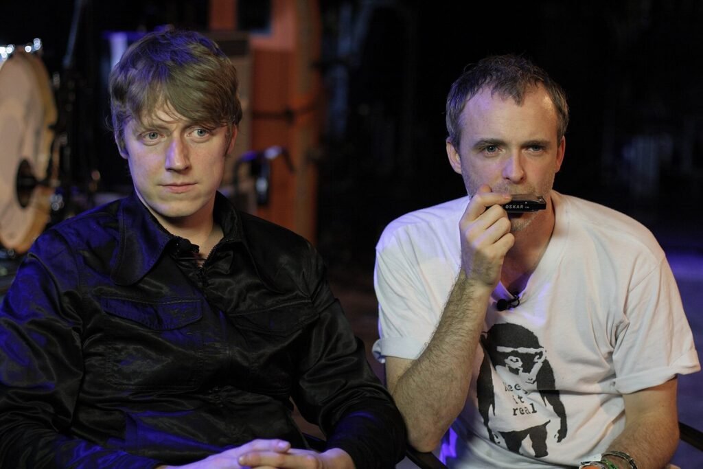 Dougie Payne y Fran Healy, de Travis, sentados en el escenario de La Riviera, en Madrid, durante una entrevista; uno de ellos toca la armónica
